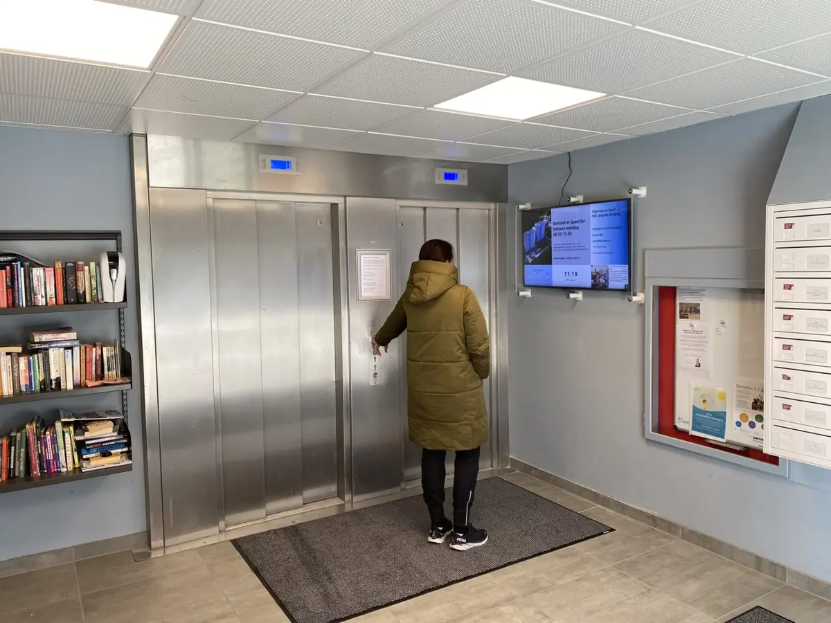 Infoskjerm på veggen ved heisene i et borettslag